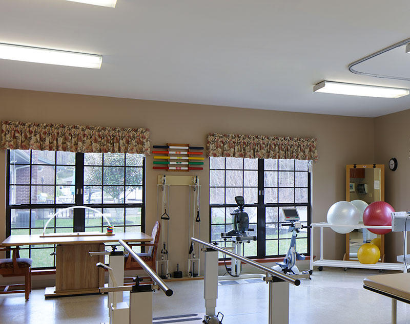 Therapy gym with parallel bars, exercise bikes, therapy balls, and weights in Madison, Virginia nursing home.