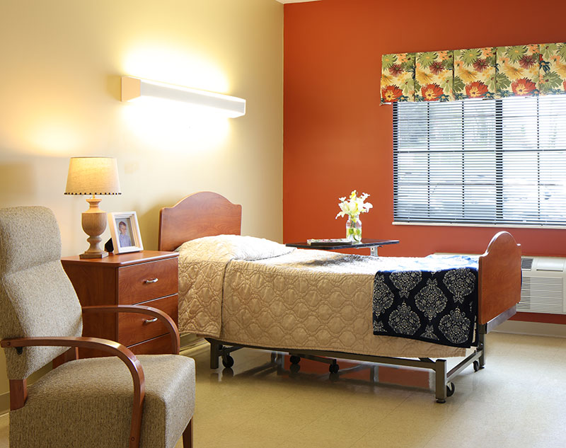 Single resident bedroom with rolling table, nightstand, and comfy chair in Madison, Virginia nursing home.