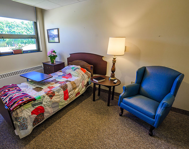 Single resident bedroom with rolling table, nightstand, and comfy chair in Ebensburg, Pennsylvania assisted living facility.